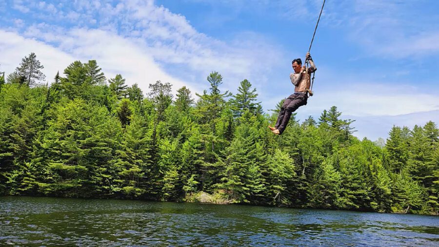 man swinging on a rope into a river