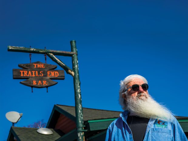 Man with white beard and sunglasses in front of the Trails End Bar