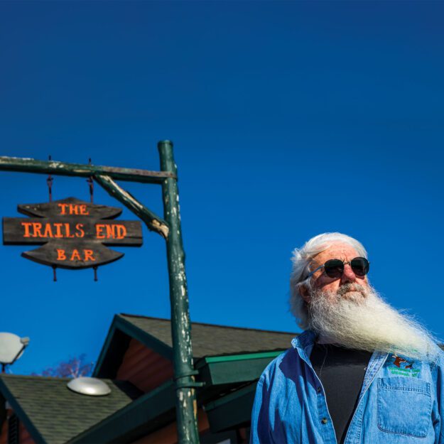 Man with white beard and sunglasses in front of the Trails End Bar