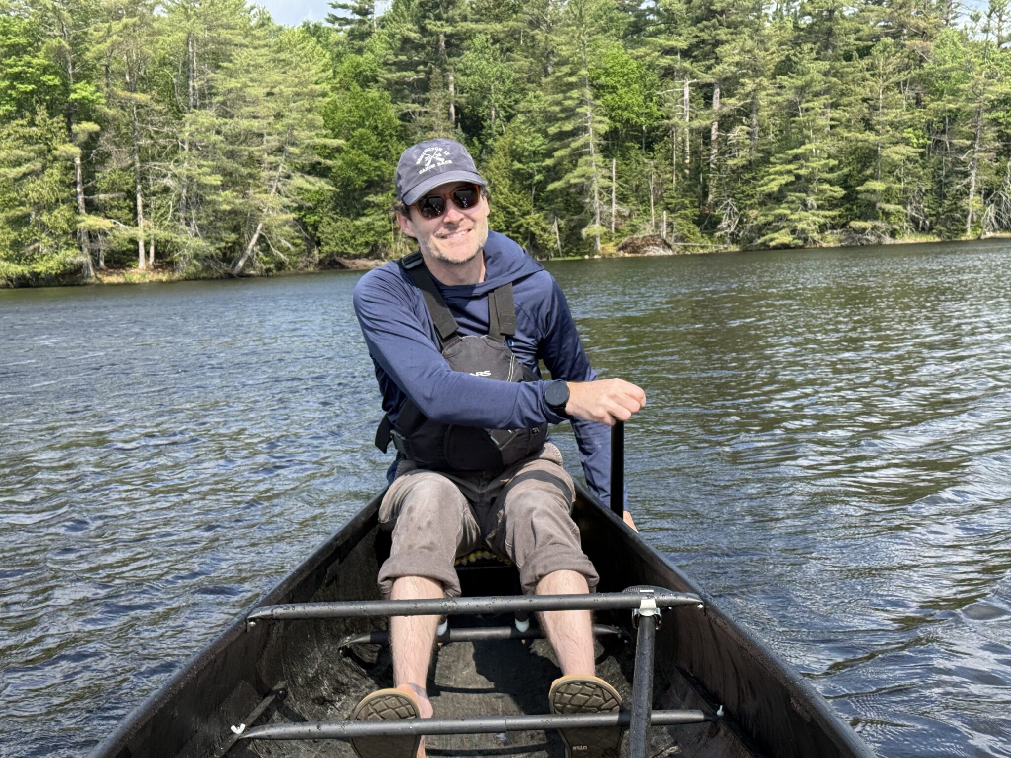 man smiling at camera while paddling a canoe