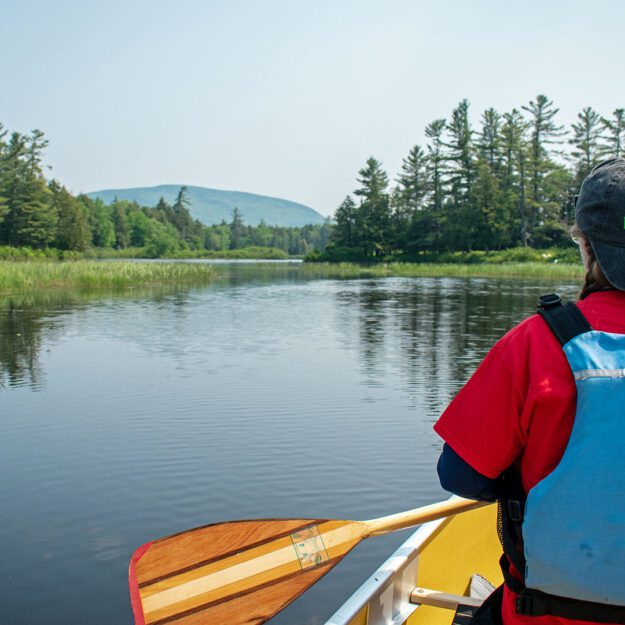woman in canoe seen from behind with paddle in hand