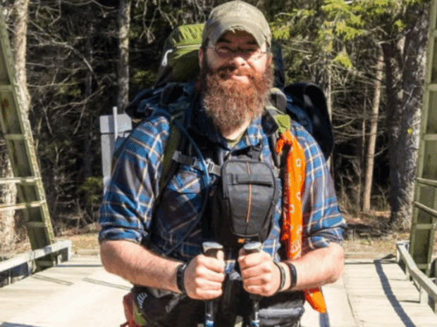 Man on bridge with hiking poles and baseball cap