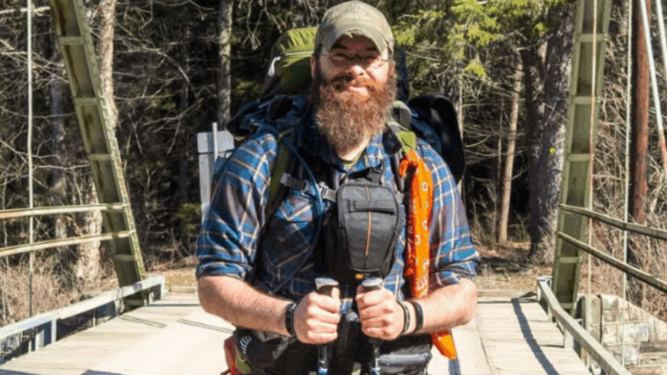 Man on bridge with hiking poles and baseball cap