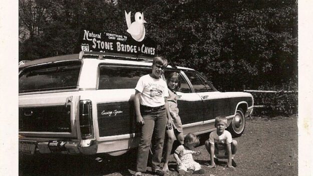 black and white photo of man and kids in front of station wagon and natural stone bridges sign