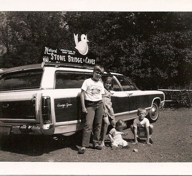 black and white photo of man and kids in front of station wagon and natural stone bridges sign