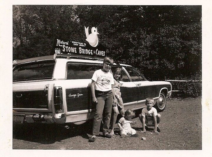 black and white photo of man and kids in front of station wagon and natural stone bridges sign