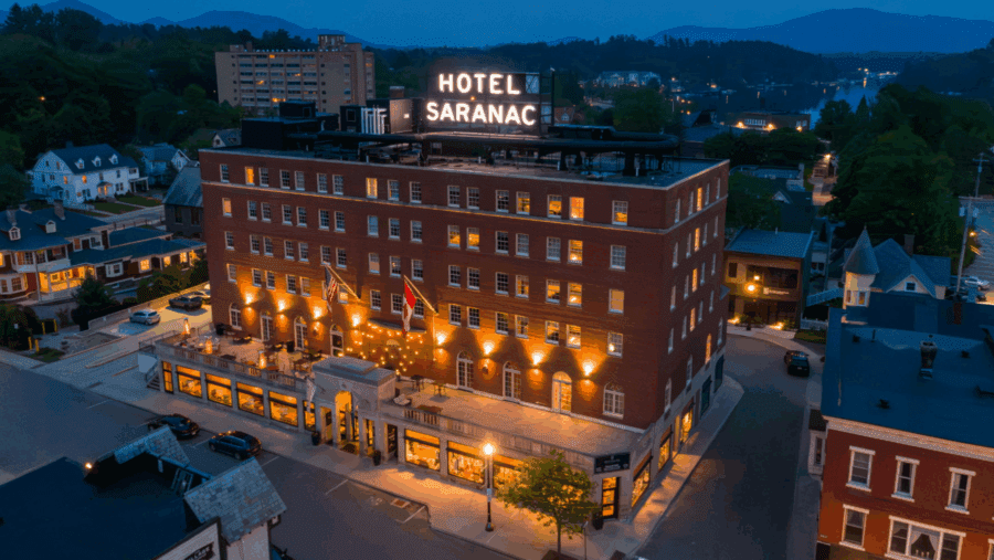 Evening aerial of Hotel Saranac in downtown Saranac Lake with mountains visible in the distance