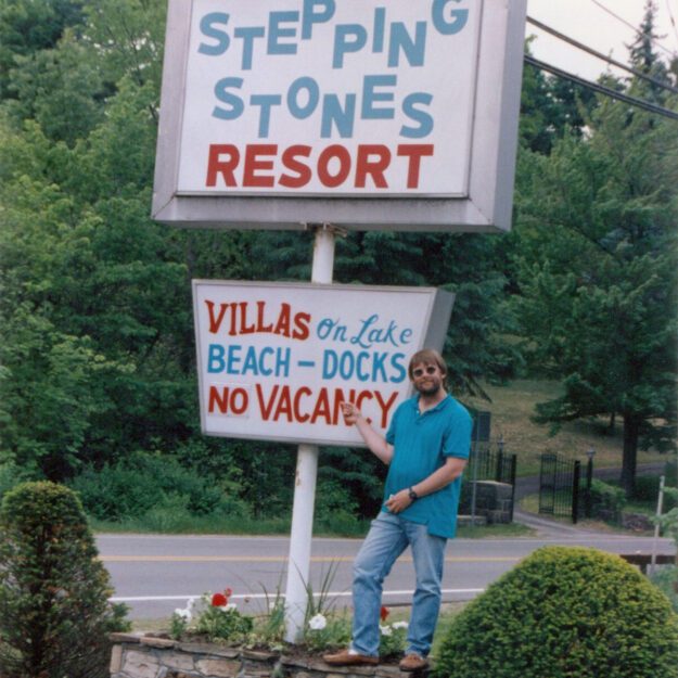 man posing with stepping stones resort sign