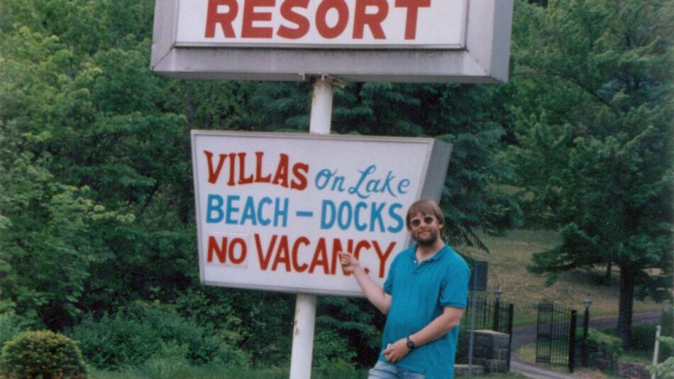 man posing with stepping stones resort sign