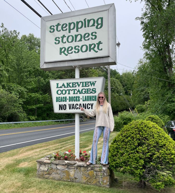 woman posing next to stepping stones resort sign