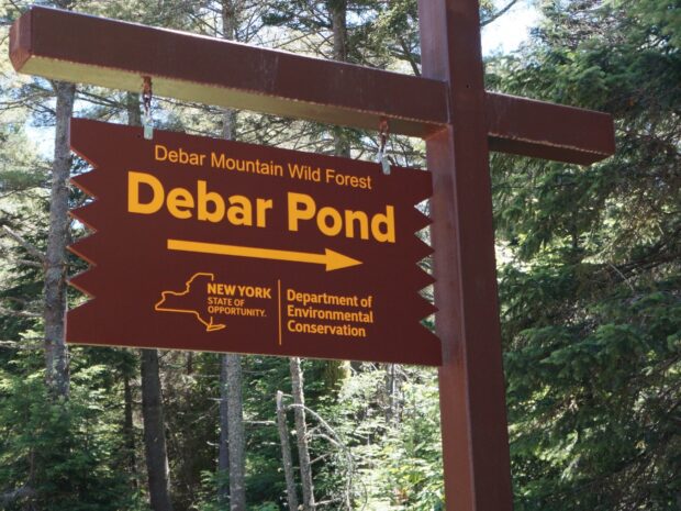 Wooden DEC sign with yellow letters and arrow that points to Debar Pond