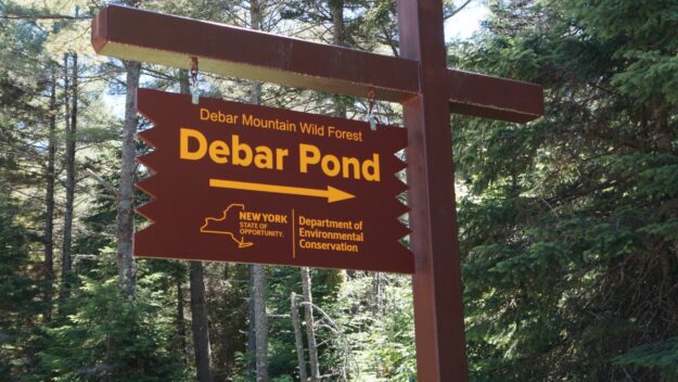 Wooden DEC sign with yellow letters and arrow that points to Debar Pond