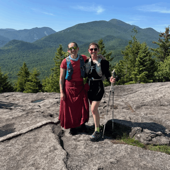 Katie Rhodes and Debbie McElwaine on Mt. Jo. dressed in red dress and black hiking outfit standing posed in front of mountain view. 