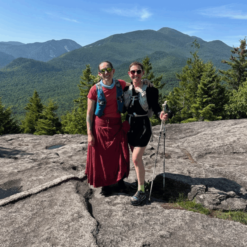Katie Rhodes and Debbie McElwaine on Mt. Jo. dressed in red dress and black hiking outfit standing posed in front of mountain view. 