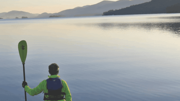 The author faces the lake paddle in hand with one end resting on the sand on the lakeshore at the start of the journey in Lake George village.
