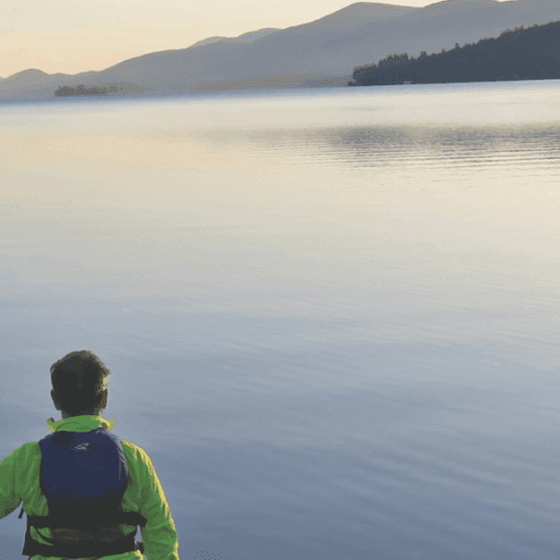 The author faces the lake paddle in hand with one end resting on the sand on the lakeshore at the start of the journey in Lake George village.