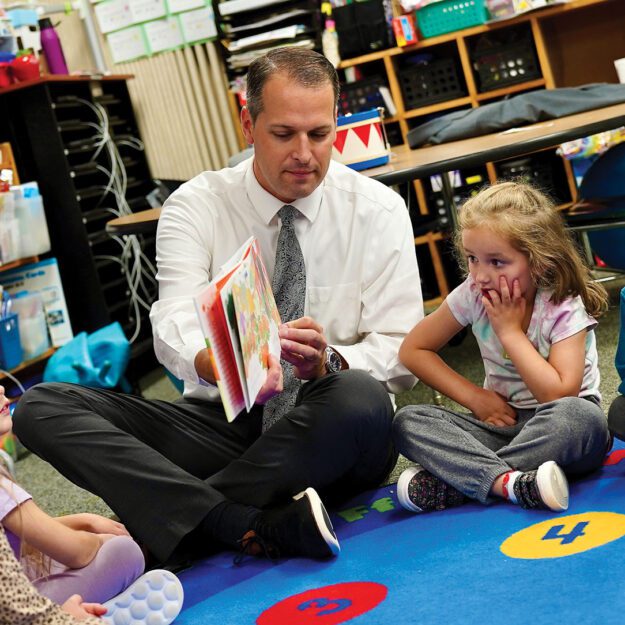 man reading to children on a colorful rug